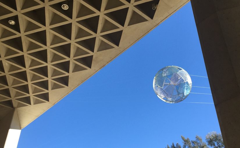 A photo of a globular sculpture suspended over a building